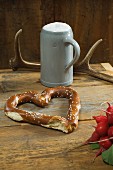 A heart-shaped pretzel with radishes, a mug of beer and antlers on a wooden table