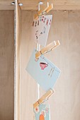 Cards with colourful motifs hung from vertical cord using clothes pegs