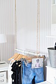 Jeans, tops and baby photo hanging on open clothes rail suspended from ropes