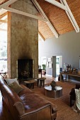 Old, brown leather sofa and low, metal table in open-plan interior with fireplace integrated in free-standing wall