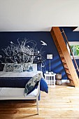 Bedroom with dark blue wall, white mural, wooden staircase and bench at foot of double bed