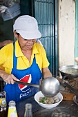 Frau serviert Nudelsuppe mit Hackbällchen in einer Strassenküche (Thailand)