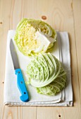 Savoy cabbage quarters on a tea towel with a knife