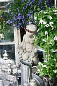 Stone statue & decorative vessels surrounded by summer flowers