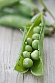 Peas in an opened pod on a wooden surface