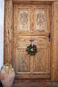Geschnitzte Zimmertür mit aufgehängtem Kranz, seitlich rustikale Bodenvase