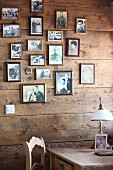 Framed family photos on wooden wall behind vintage table lamp on table