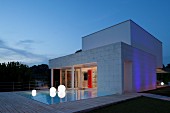 Twilight atmosphere; pool, spherical floor lamps and wooden deck outside contemporary house