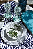 Place setting with blue and white patterned crockery, olive twig and ikat tablecloth