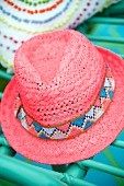 Pink straw hat with patterned hat band on green wicker chair