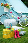 Pink Wellington boots next to yellow picnic basket in front of white pouffe and decorated bicycle in front of blue tent