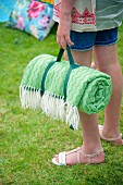 Rolled, green picnic blanket held by girl in garden