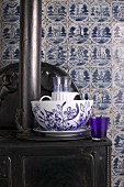 Blue and white crockery on antique cast iron stove against old wall tiles in classic Delft blue and white