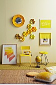 Still-life arrangement of small, yellow table and yellow-painted, retro chair below cake tins and pictures on pastel yellow wall