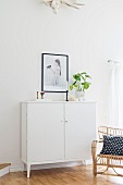 White, half-height cabinet, black-framed picture and wicker armchair with black and white scatter cushion
