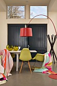 Dining table, blankets draped on classic chairs, red designer arc lamp and coat stand in background