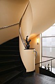 Elegant, curved staircase with black stone steps, chrome handrail and sculpture on newel