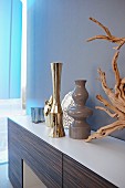 Elegante Vasen verschiedener Stilrichtungen und dekorative Wurzel auf Sideboard mit Edelholzfront