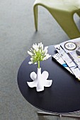 White allium in white, designer vase formed as inverted china flower next to stack of magazines on side table