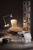 Designer Sessel mit Fussschemel zwischen Tischleuchte auf Klapptisch und Bücherregal