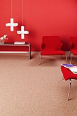 Red lounge chairs, white, cross-shaped pendant lamps and side table against red wall