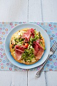 Pizza with ham, rocket, tomatoes and pine nuts