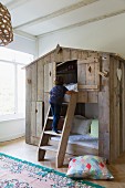 Two children's cubby beds in rustic wooden house with child climbing ladder; Oriental rug and large cushion on floor