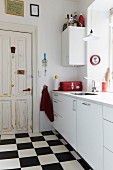 Simple, white fitted kitchen with black and white chequered floor