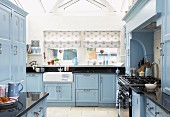 Pale blue, country-house kitchen with counter below windows with patterned Roman blinds