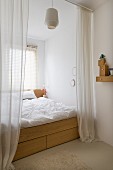 Floor-length open curtains screening double bed with drawers in wooden frame built into window niche