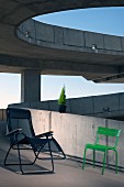 Metal tube lounger with mesh seat and grass green outdoor chair on ramp of concrete building