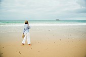 Frau geht telefonierend am Strand entlang (Camaret-sur-Mer, Frankreich)