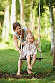 Mutter mit Tochter beim Schaukeln im Garten