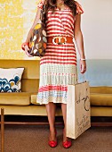 Woman wearing striped summer dress carrying polka-dot bag in front of mustard retro velvet sofa