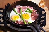 Two fried eggs with ham and asparagus in a cast iron pan