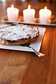 Pie dusted with icing sugar in front of lit candles