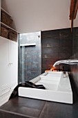 Designer sink against wall with dark metallic tiles and shower area in background