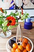 Designer bowl of fruit and bouquet with gerbera daisies on dining table