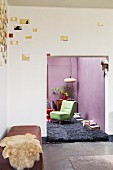 Artistic wall decoration above sheepskin blanket on bench in corner; view into living room with purple walls