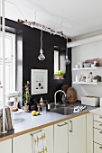 White kitchen counter against black wall with window and creative lamps