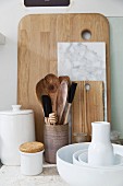 White crockery and various wooden spoons in jar in front of chopping boards