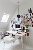 Ghoststuhl mit weißem Schaffell vor Schreibtisch und aufgeklebten Fotos an Wand, Dachschräge mit Dachflächenfenster