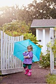 Little girl walking in garden carrying umbrella