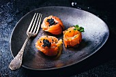 Salmon rolls with black caviar on a plate with a fork