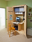 Wooden chair in front of DIY, open office cabinet with integrated desk, monitor and box files