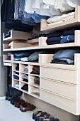 Open-fronted wardrobe with clothing hung from rail and drawers in dressing room