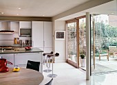 Küche mit Fronten aus gebürstetem Aluminium und Barhocker Lem von Shin und Tomoko Azumi an Kücheninsel; Fensterfront zur Terrasse; vorne runder Esstisch