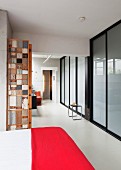 Bed with red bedspread in open-plan interior opposite frosted glass wall with black, steel frame