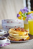 A stack of buttermilk pancakes with pecan nuts and maple syrup