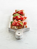 Three slices of bruschetta with basil on a wooden board